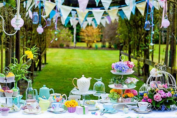 An elegant outdoor tea party setup with teapots, cakes, and colorful decorations.