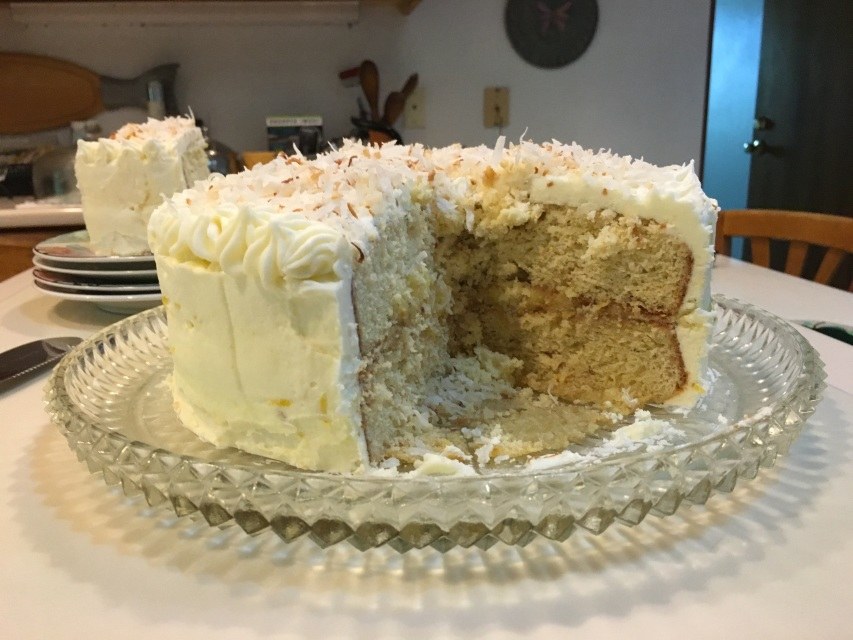 A partly eaten layered cake with white frosting on a glass plate.