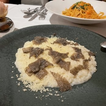 Creamy risotto topped with shaved truffles on a black plate.