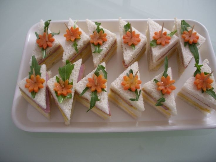 Triangular sandwiches garnished with carrot flowers and green leaves.