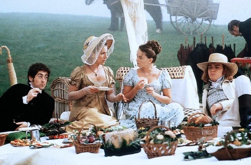 People dressed in vintage clothing enjoying a picnic outdoors.