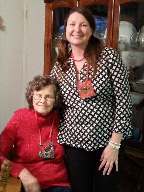 Two women smiling indoors, one seated and one standing.