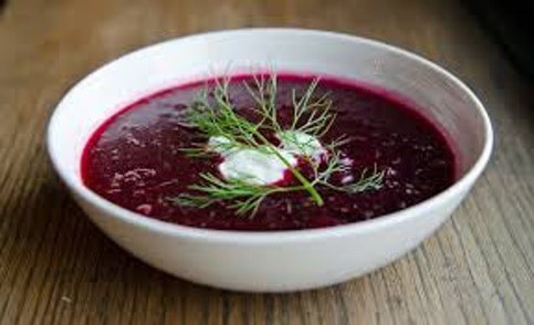 A bowl of vibrant beet soup garnished with cream and dill.
