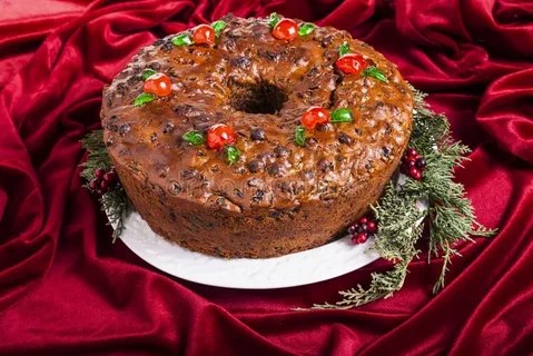 Festive fruitcake adorned with cherries and nuts on a white plate.