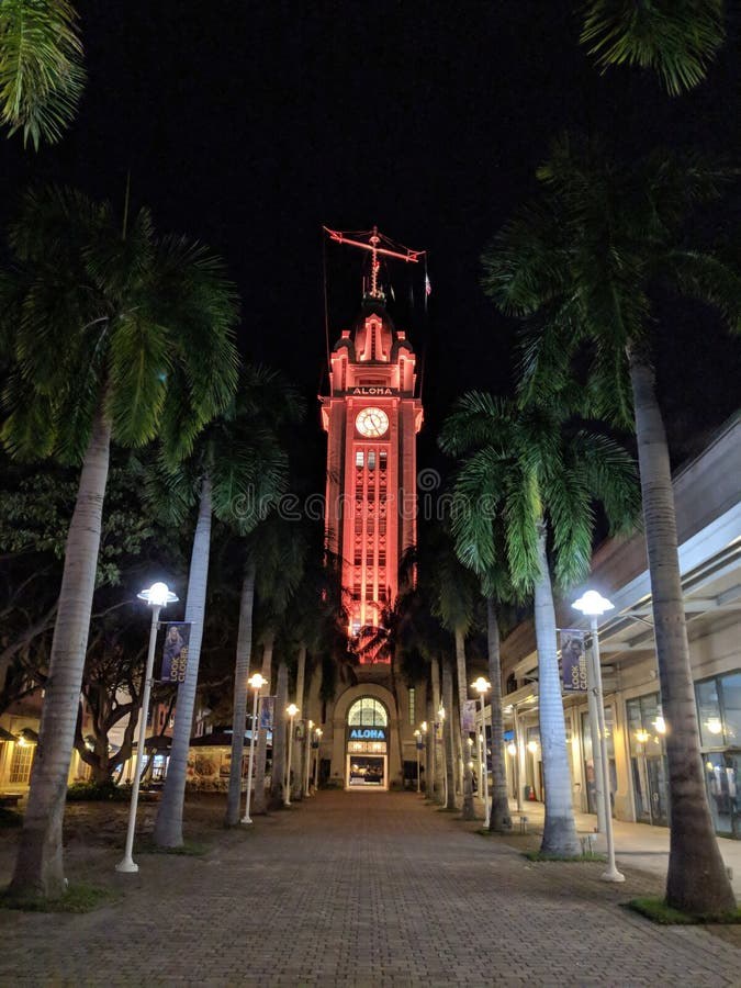 A tall clock tower illuminated in red at night, framed by palm trees.