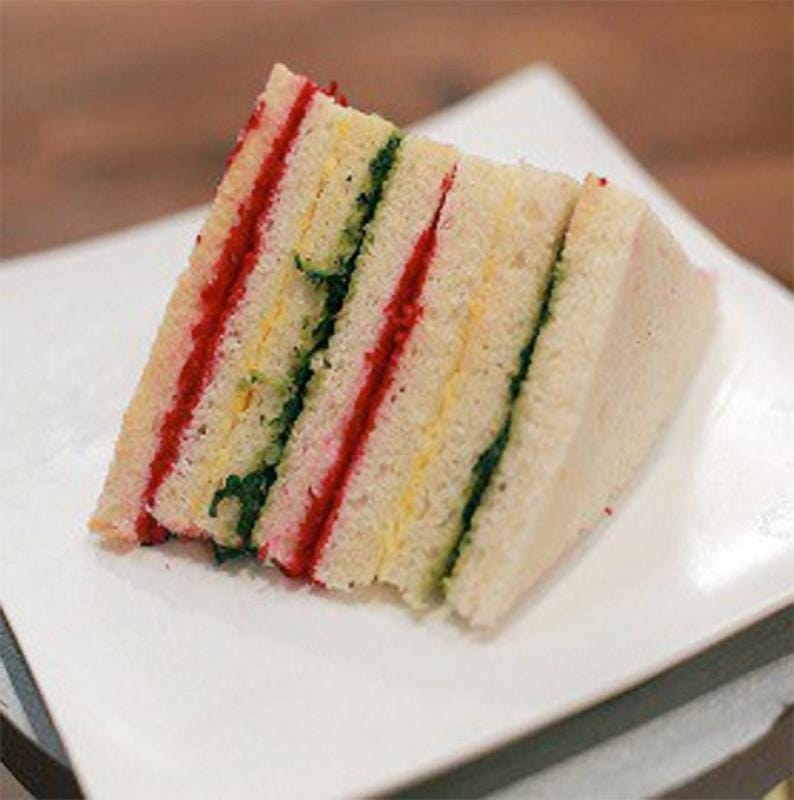 Triangular tea sandwich with layers of cucumber and tomato.