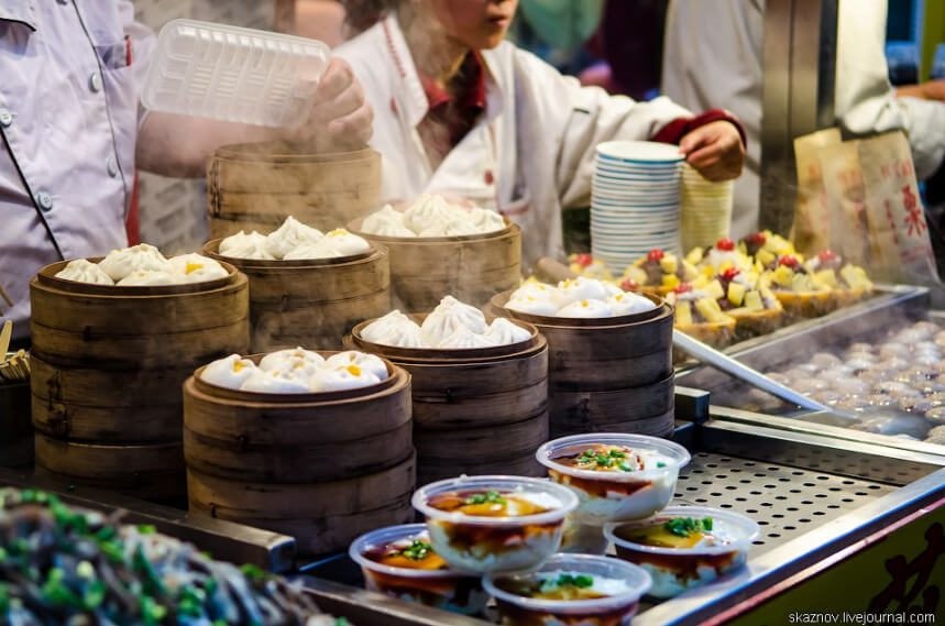 Stacked bamboo steamers filled with dumplings at a busy food market.