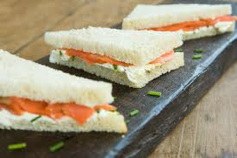 Triangular smoked salmon tea sandwiches on black slate.