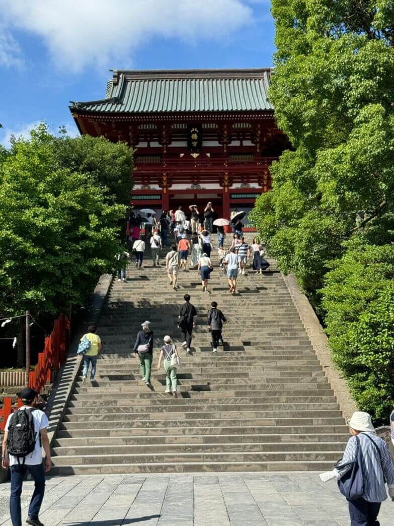 Visitors climbing stairs at a traditional Japanese temple entrance surrounded by greenery.