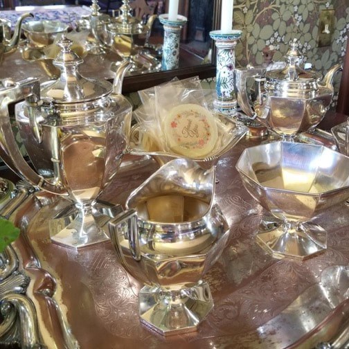A polished silver tea set with intricate designs on a reflective tray.