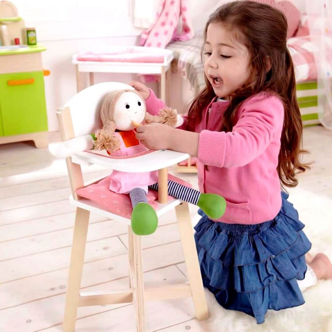 A young girl feeding a stuffed dog in a toy high chair.