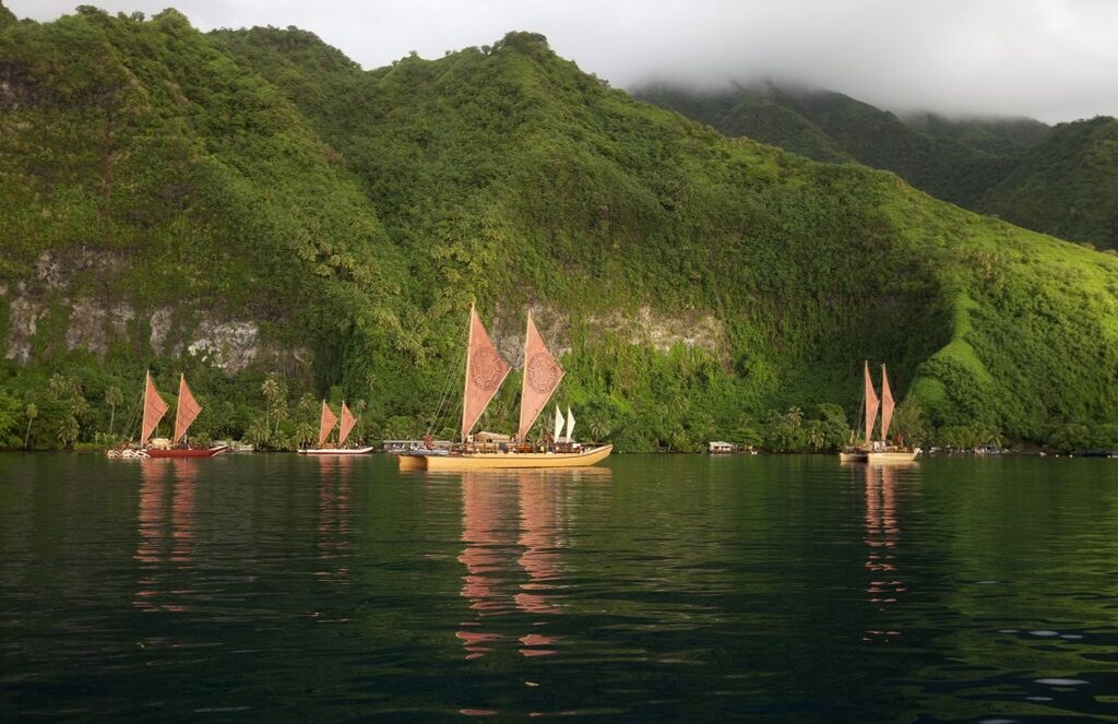 Traditional sailboats on calm water near lush green mountains.