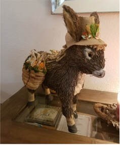 Handcrafted donkey figure carrying a basket with plants.