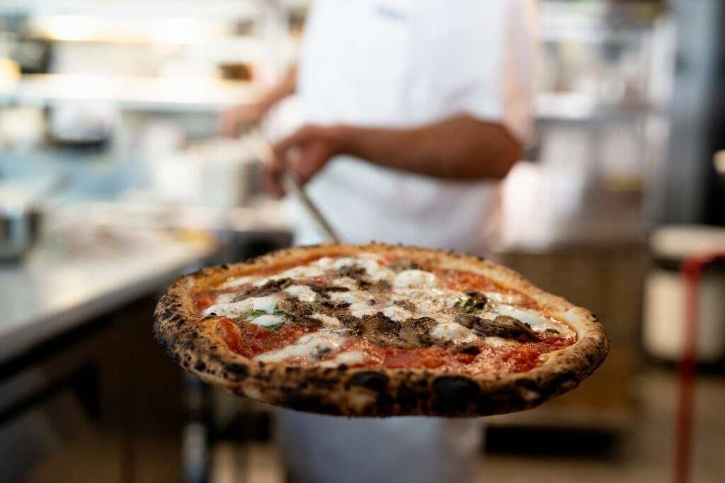 A freshly baked pizza with toppings being held out.