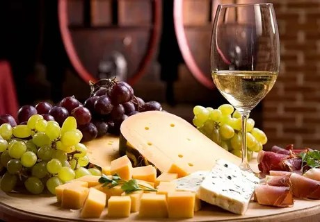 Cheese platter with grapes and wine glass in front of barrels.