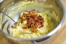 Creamy mashed potatoes topped with crispy bacon bits in a mixing bowl.
