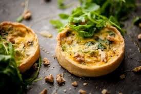 Two savory mini quiches garnished with fresh greens on a rustic surface.