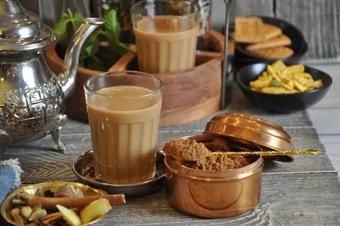 A cup of Indian chai tea served with a container of tea powder and snacks.