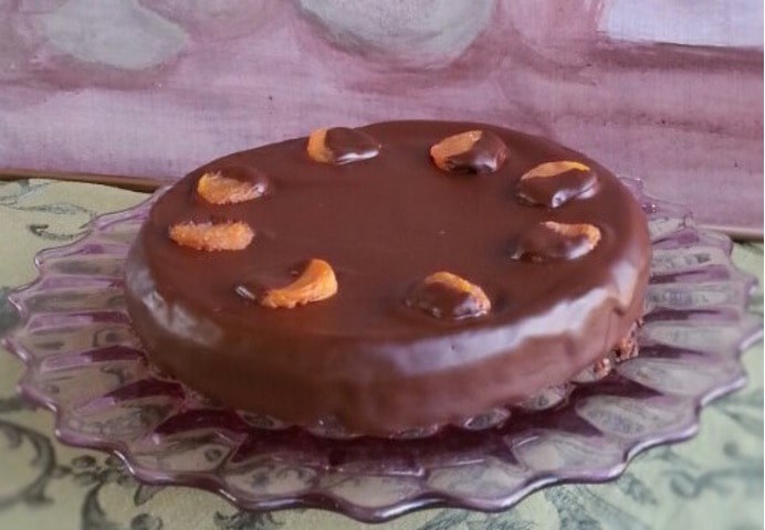 A chocolate cake topped with cashew nuts on a glass plate.