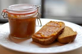 A jar of orange marmalade with bread slices spread with marmalade.
