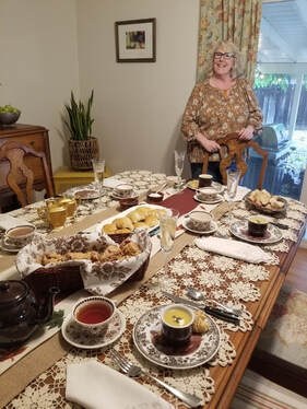 A woman sits by a dining table filled with various dishes and tea cups.