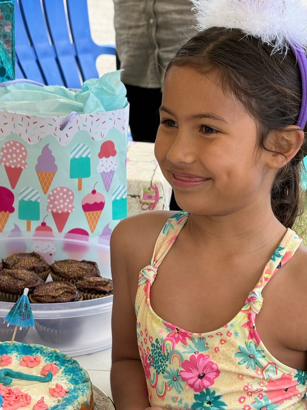A smiling girl in a colorful dress stands next to a table with cookies and an ice cream-themed tablecloth.