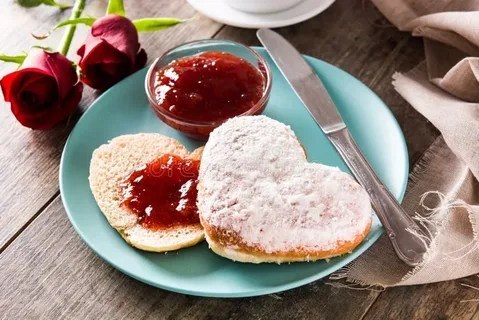 Heart-shaped pancakes, one dusted with powdered sugar, the other topped with jam.