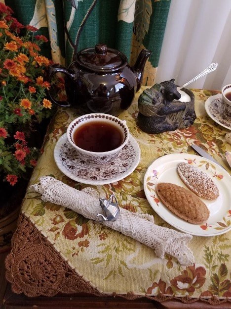 A cozy tea setup with a cup of tea, cookies, and a rustic stick on a floral tablecloth.