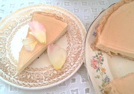 A slice of cheesecake with rose petals on a decorative plate.