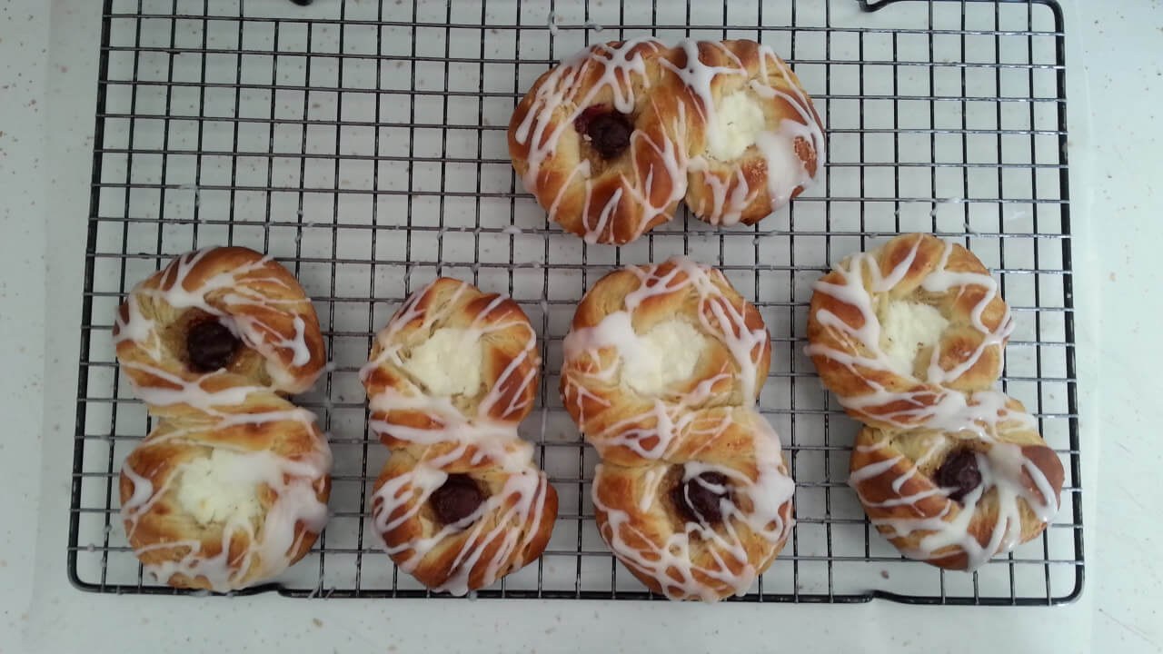 Freshly baked pastries with icing on a cooling rack.