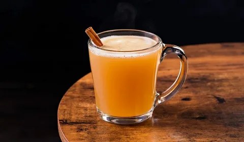 A warm glass mug of spiced apple cider with a cinnamon stick.