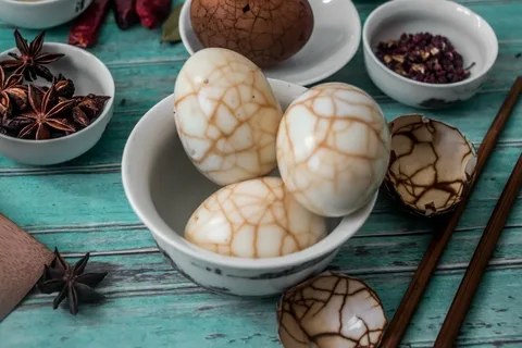 Three marbled eggs in a white bowl on a turquoise wooden table.