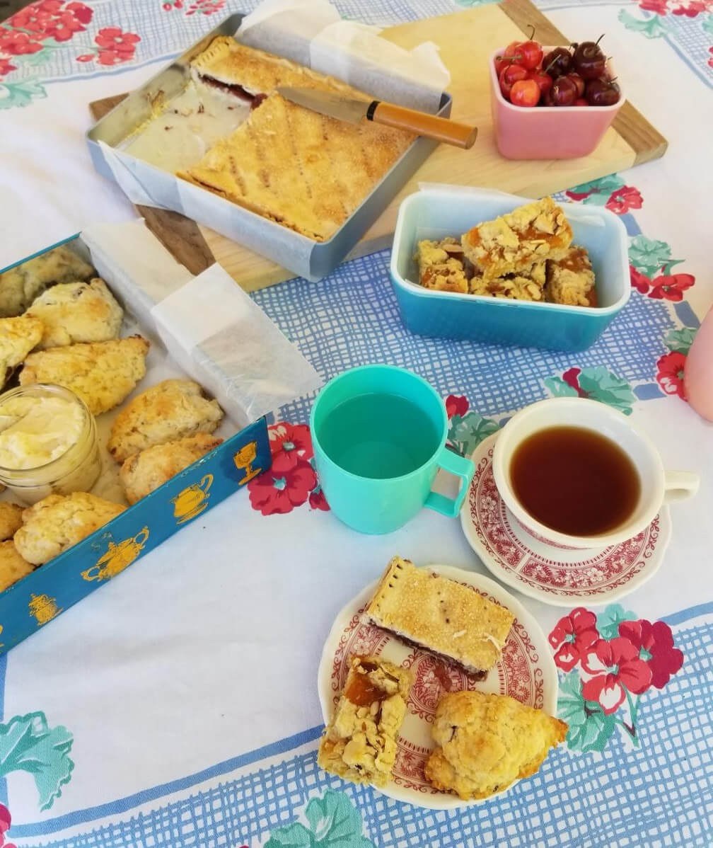 A cozy tea setup with crackers, cheese, and pastries on a floral tablecloth.