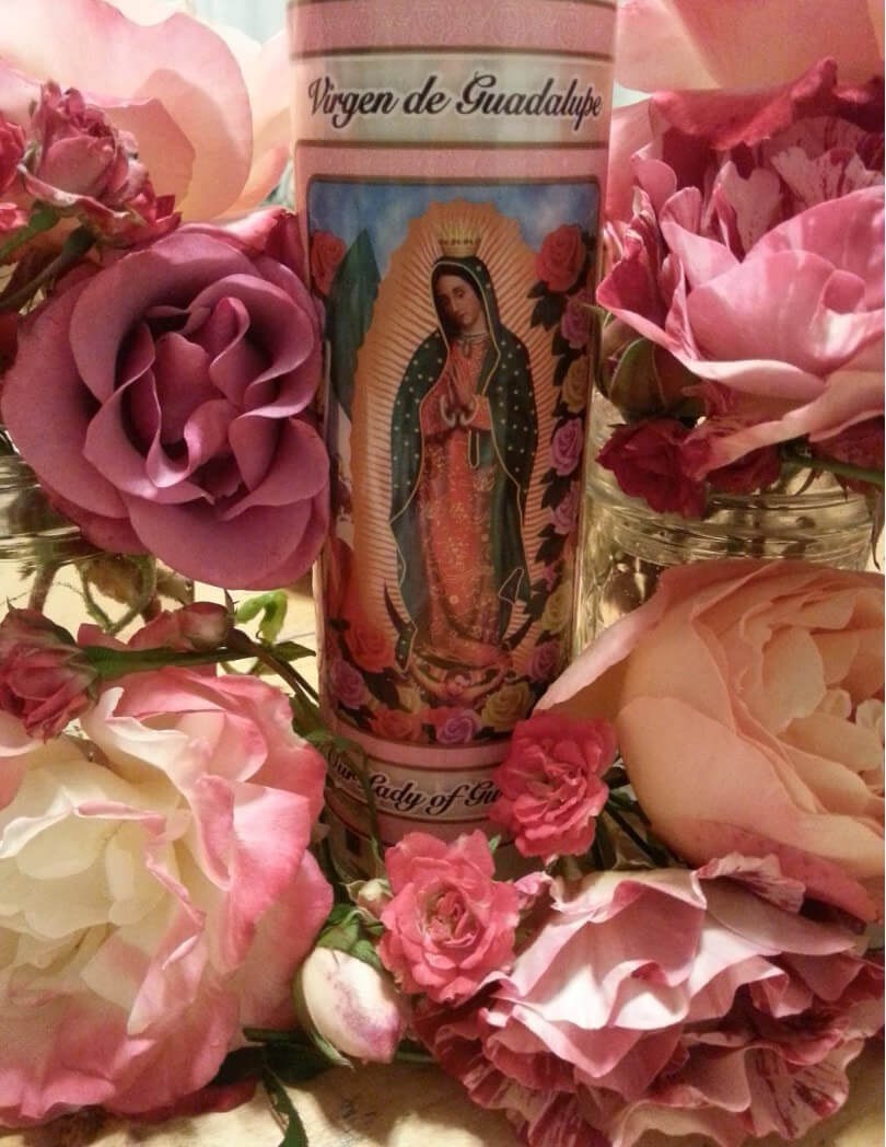 Religious candle surrounded by pink roses.