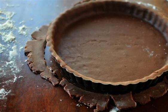 A chocolate tart crust in a tart pan on a wooden surface.