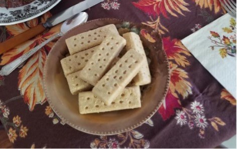 A plate of rectangular shortbread cookies with holes on a floral tablecloth.