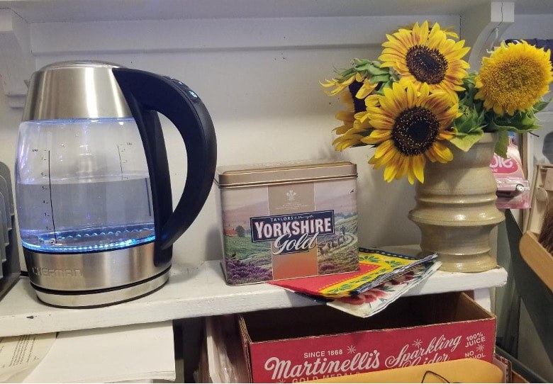 Electric kettle beside Yorkshire tea and sunflowers on a kitchen shelf.