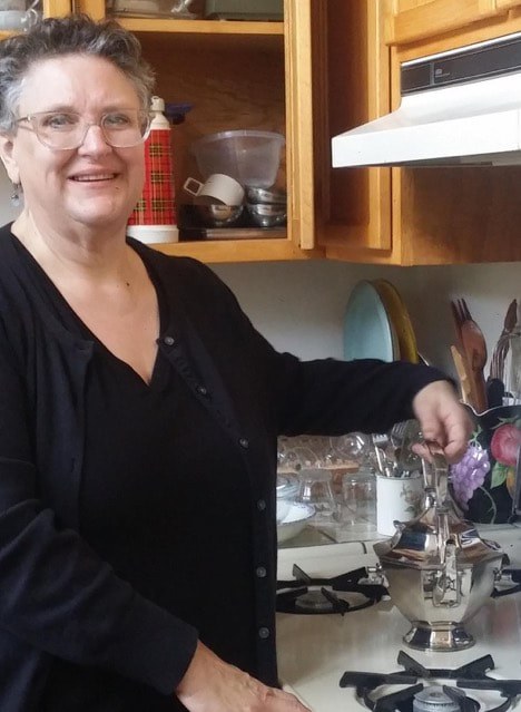 A smiling woman prepares tea in a cozy kitchen.