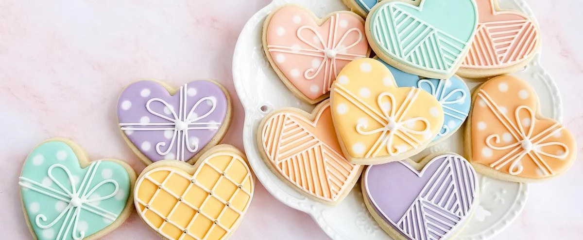 Colorful heart-shaped cookies with intricate icing designs on a white plate.