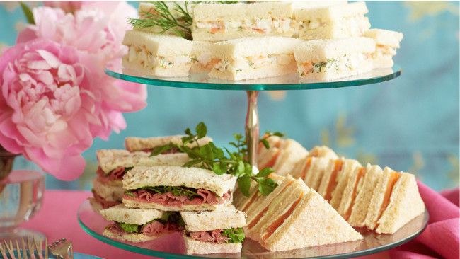 Assorted tea sandwiches arranged on a glass tiered tray.