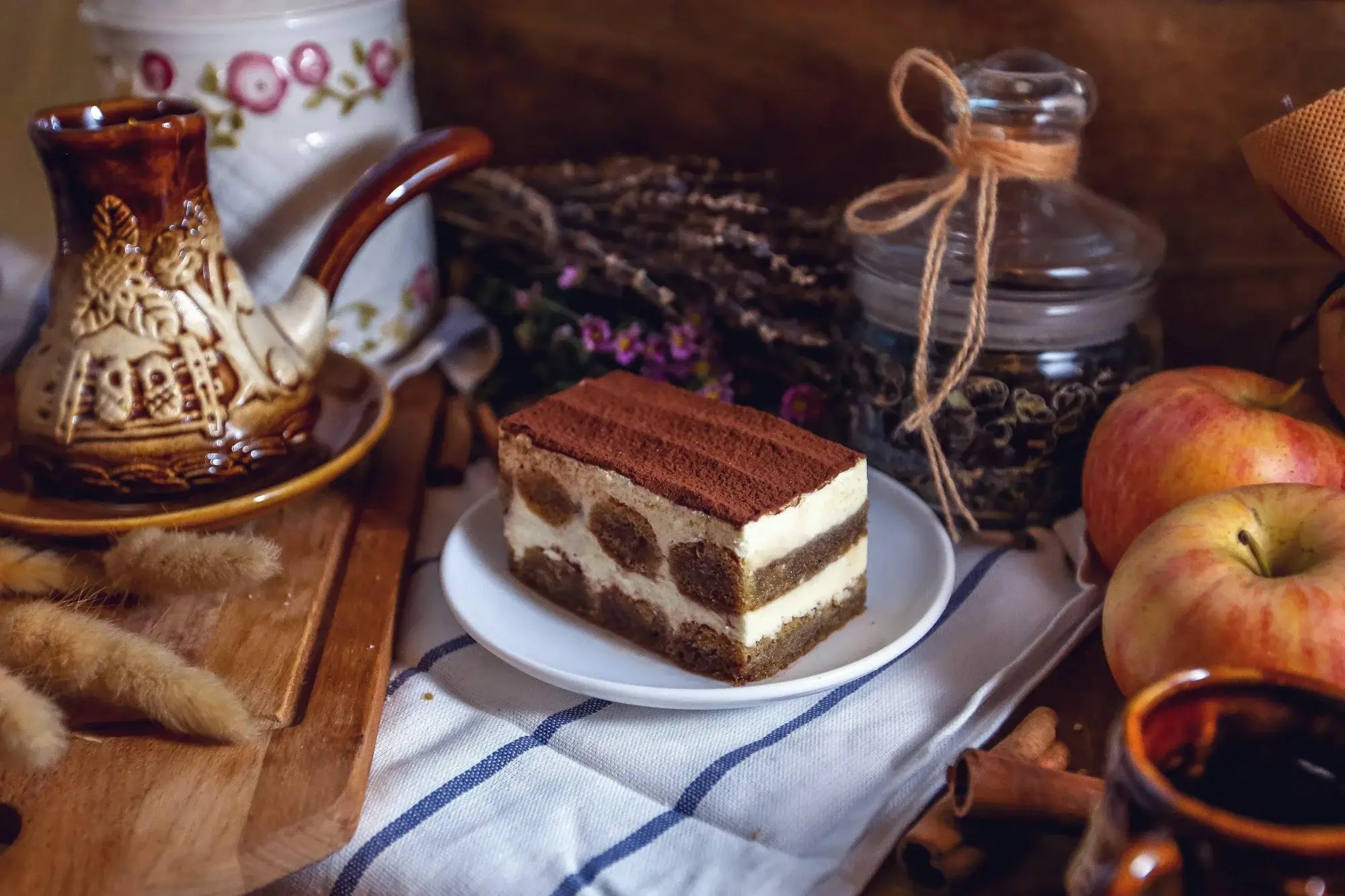 Slice of tiramisu on a rustic table with coffee and cinnamon sticks.