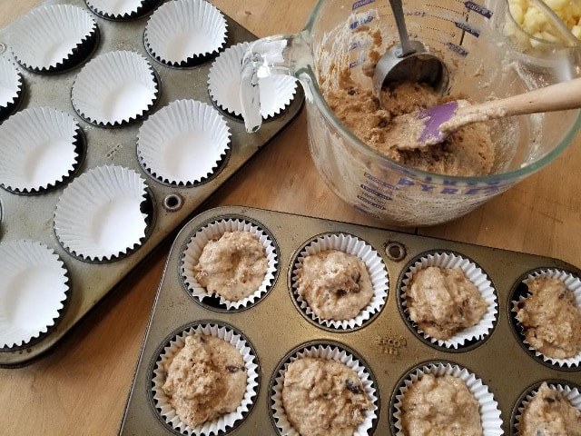 Scooping muffin batter into paper liners in a muffin tin.