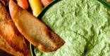 Crispy pita bread served with creamy green hummus on a plate.