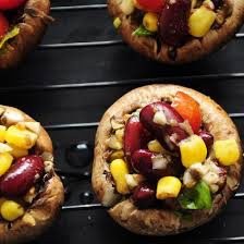 Colorful stuffed mushrooms with beans, corn, and herbs on a grill.