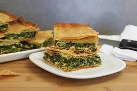 A slice of spinach pie on a white plate with more pie in the background.