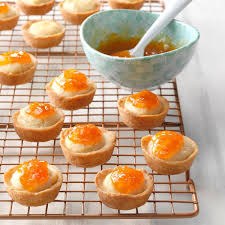 Mini tartlets topped with orange marmalade on a cooling rack.