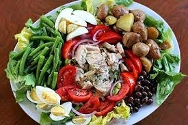 A colorful salad with chicken, tomatoes, green beans, potatoes, olives, and boiled eggs.