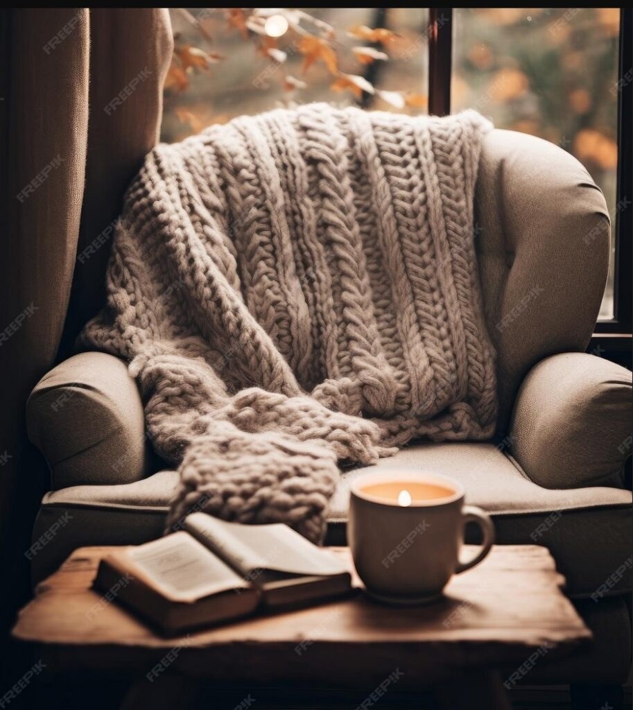 Cozy armchair with knitted blanket, book, and coffee cup in warm light.