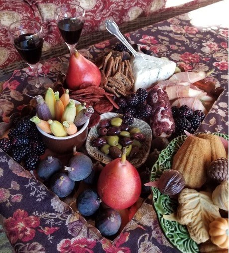 A rich spread of fruits, nuts, breads, and wine on a patterned tablecloth.
