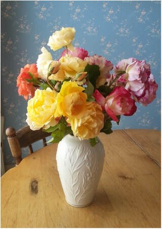 A vibrant bouquet of multicolored roses in a white vase on a wooden table.